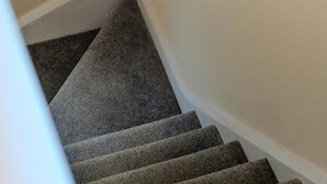 Eine Teppichstufen Treppe mit Handlauf, weißen Wänden und zwei gerahmten Bildern.