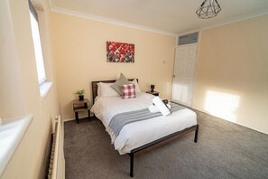 A bedroom with a bed, bedside tables, a window, and a door. - Comfortable 4-bed Home With Free Parking (Swansea)