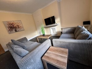 A living room with a sofa, a coffee table, and a television on a stand. - Comfortable 4-bed Home With Free Parking (Swansea)
