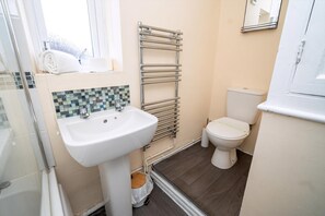 A bathroom with a white sink, a toilet, a towel rack, and a shower area. - Comfortable 4-bed Home With Free Parking (Swansea)