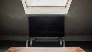 Una stanza con un lucernario, una TV a schermo piatto su un supporto e un tavolo in legno.