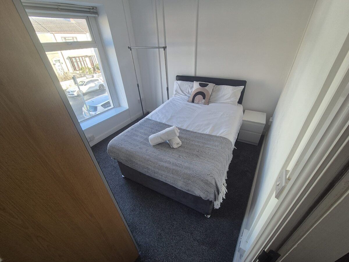 Ein Hotelzimmer mit Bett, Fenster mit Blick auf geparkte Autos und einer Tür zu einem weiteren Raum.