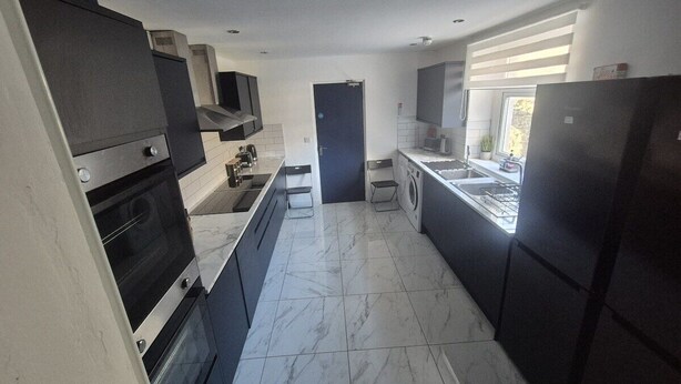 Una cucina moderna con mobili scuri, forno integrato, lavatrice e una finestra che lascia entrare luce naturale.