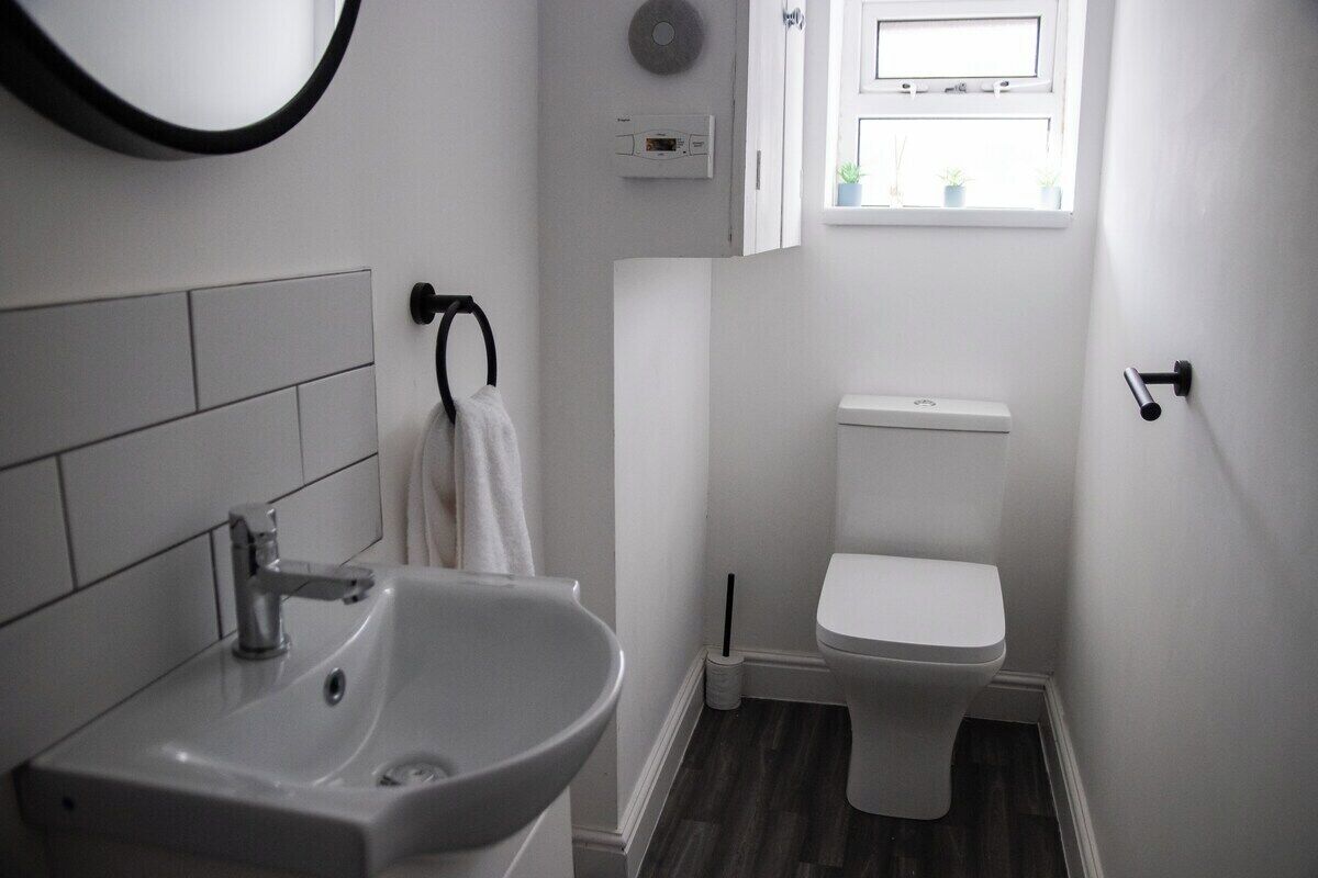 Et badeværelse med en hvid vask, toilet og et lille vindue med planter.