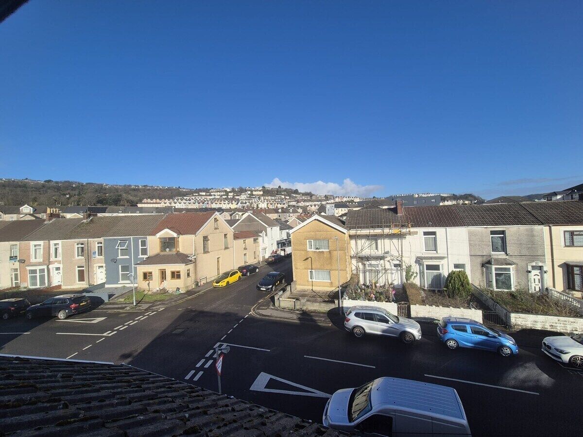 A residential street with houses, parked cars, and a clear blue sky.