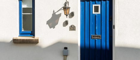 A building with a blue door, a window with a blue frame, and a wall-mounted light fixture.
