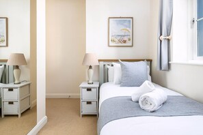 Un dormitorio ordenado con cama, mesitas de noche, lámparas y un cuadro en la pared.
