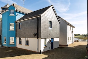A two-story building with a blue and white facade, a visible door, and a paved courtyard. - Seaview 2-bed With Private Parking, Portishead (Bristol)