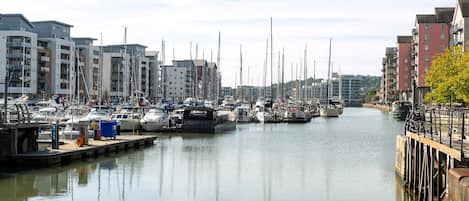 Un port de plaisance où sont amarrés de nombreux bateaux, une voie navigable et des bâtiments de part et d’autre.
