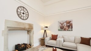 Ein Wohnzimmer mit Kamin, einer Couch, einem Couchtisch und einer Wanduhr.