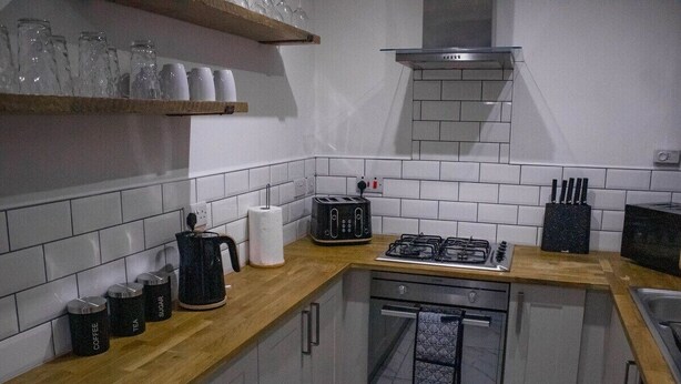 A compact kitchen with a gas stove, toaster, and coffee maker on the counter. - Spacious & Comfortable 2-bedroom Home (Swansea)