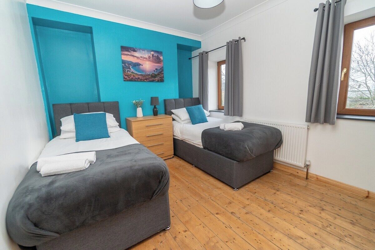 Un dormitorio con dos camas, piso de madera, pared de acento azul y una ventana con cortinas.