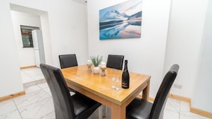 A dining area with a wooden table, black chairs, a painting on the wall, and a bottle of champagne. - Spacious & Comfortable 2-bedroom Home (Swansea)