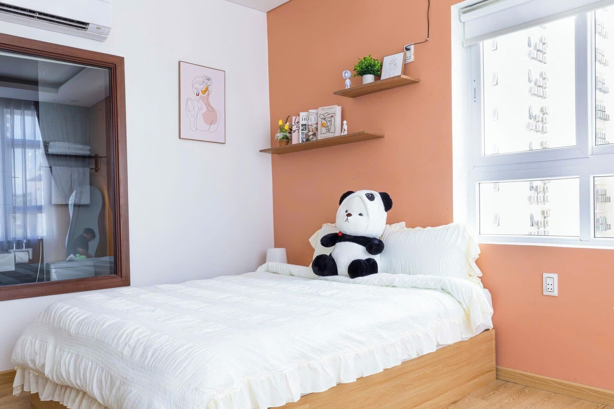 Une chambre avec un lit, une fenêtre, une étagère fixée au mur avec quelques objets et un ours en peluche à l’effigie d’un panda.