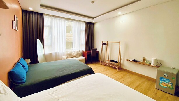 A hotel room with a bed, a chair, a desk, a hanging clothes rack, and a minibar. - BEAR HOTEL & HOMESTAY 2 (Da Nang)