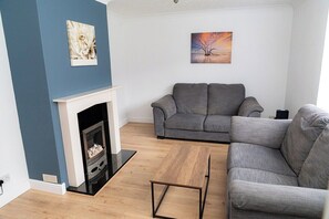 A modern living room with a grey sofa, a wooden coffee table, and a fireplace. - Comfortable 3-bed, 2-bath Basingstoke Stay (Basingstoke)