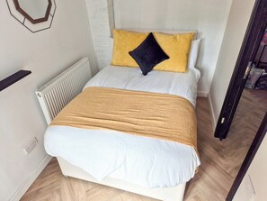 Ein ordentlich bezogenes Bett mit einer weißen und goldenen Decke, einem schwarzen Kissen und einem gelben Kissen.
