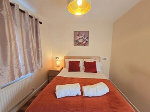 A hotel room with a bed, a nightstand, a lamp, and a window with curtains. - Bright 4-bed Swansea Getaway With Parking (Swansea)