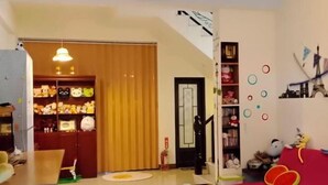 A cozy living room with a red sofa, a wooden coffee table, and a bookshelf filled with plush toys. A wooden door leads to another room, and a small table with a lamp is visible in the corner. - One of seven BnB (Hualien)