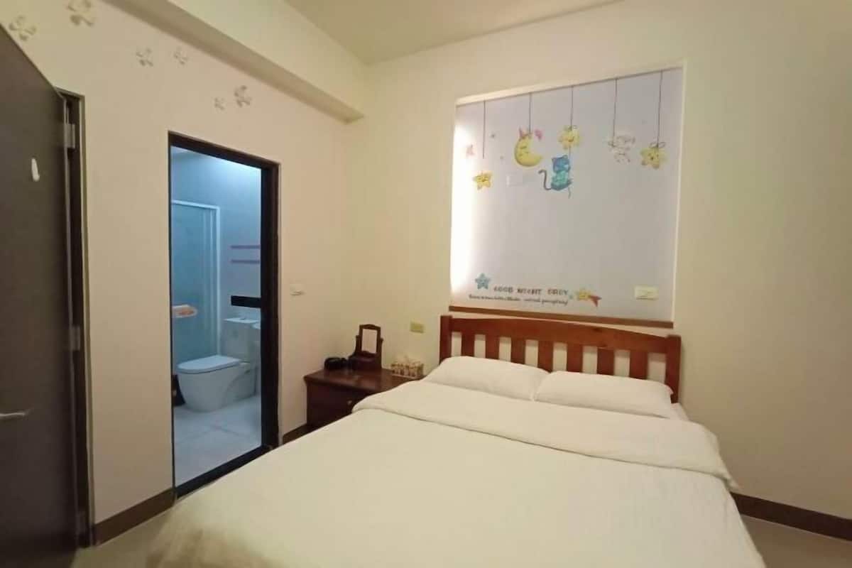 A bedroom with a bed, a wooden headboard, a nightstand, and a wall decoration.