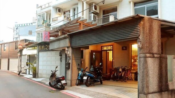 A building with a ground-level entrance, a signboard, and parked scooters. - One of seven BnB (Hualien)