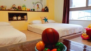 A hotel room with two beds, a window with curtains, a wall decorated with children's toys, and a table with a bowl of fruit and a basketball. - One of seven BnB (Hualien)