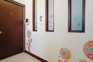 A hallway with a wooden door marked '7A', a wall-mounted intercom, and decorative floral wall stickers. - One of seven BnB (Hualien)