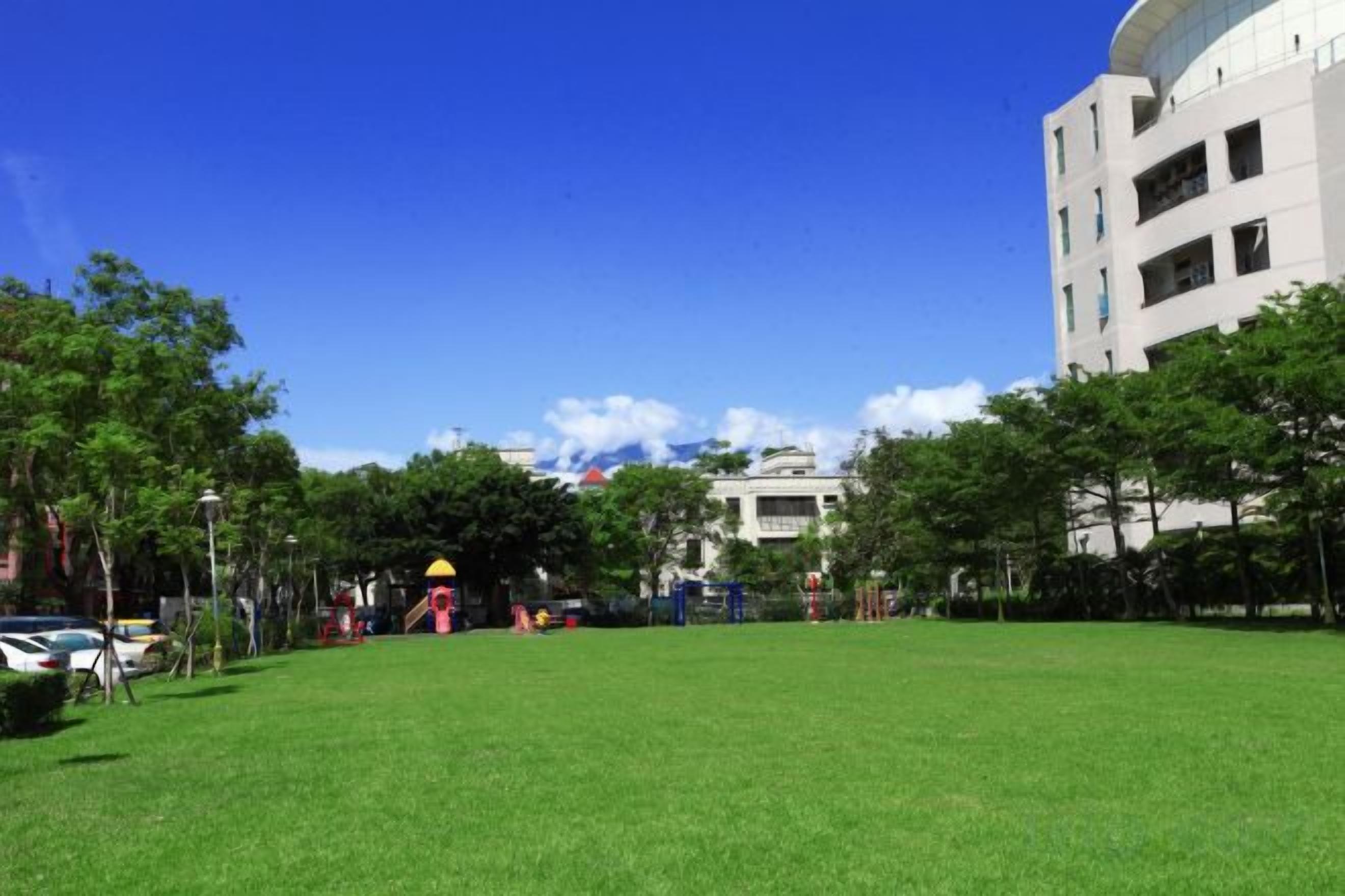 A grassy courtyard with a playground, trees, and a building in the background.