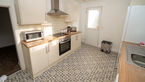 A compact kitchen with white cabinets, a microwave, a stove, and a sink. - Cosy 3-bed House Walk to Swansea Stadium (Swansea)