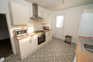 A compact kitchen with white cabinets, a microwave, a stove, and a sink. - Cosy 3-bed House Walk to Swansea Stadium (Swansea)