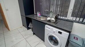 Eine kleine Küche mit Waschmaschine, Spüle und einem Fenster mit Jalousien.
