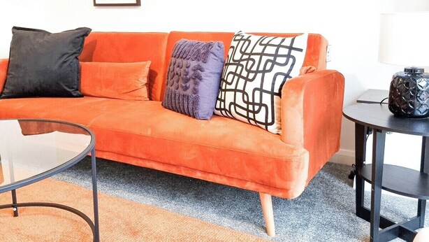 Ein modernes Wohnzimmer mit einem orangefarbenen Sofa, einem Glastisch und einem schwarzen Beistelltisch.