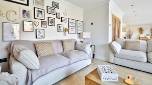 Ein Wohnzimmer mit grauem Sofa, einem Holztisch und einer Wand mit gerahmten Fotos und inspirierenden Zitaten.