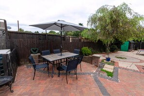A patio with a table and chairs, a large umbrella, and a brick floor. - The Swansea Homestay Spacious 4-bed Retreat (Swansea)