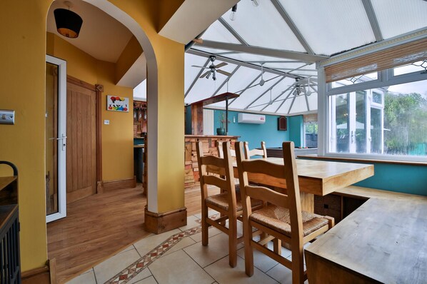 A dining area with a wooden table and chairs, a ceiling fan, and a view through a large window. - The Swansea Homestay Spacious 4-bed Retreat (Swansea)