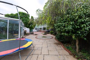 A backyard with a trampoline, a covered patio area, and a fenced garden. - The Swansea Homestay Spacious 4-bed Retreat (Swansea)