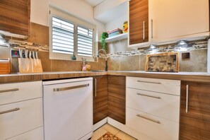 A modern kitchen with wooden cabinets, a dishwasher, and a window with blinds. - The Swansea Homestay Spacious 4-bed Retreat (Swansea)