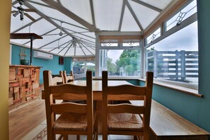 A conservatory with wooden chairs and a table, large windows, and a view of the outside. - The Swansea Homestay Spacious 4-bed Retreat (Swansea)