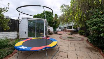 A trampoline in a backyard with a small shed and a paved pathway.