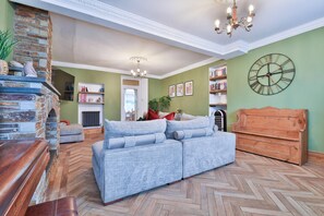 A living room with a sectional sofa, a wooden bench, a stone fireplace, and a large wall clock. - The Swansea Homestay Spacious 4-bed Retreat (Swansea)