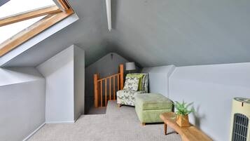 A room with a sloped ceiling, a wooden bench, a green upholstered chair, a small table with a plant, and a radiator.