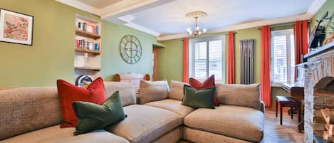 A living room with a sectional sofa, a fireplace, a bookshelf, and a clock on the wall.