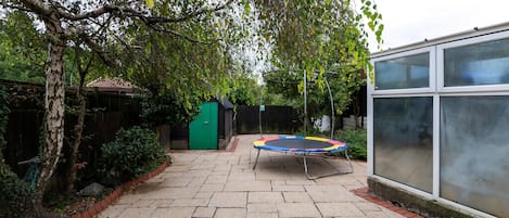 A backyard with a trampoline, a green door, and a large windowed structure.