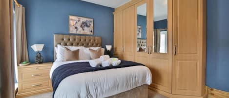 A bedroom with a large bed, a wardrobe, a nightstand, and a lamp.