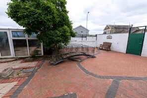 A paved courtyard with a brick pathway, a metal fence, a bench, and a green gate. - The Swansea Homestay Spacious 4-bed Retreat (Swansea)