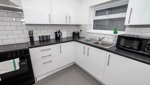 A modern kitchen with white cabinets, a black countertop, a stove, a sink, and a microwave. - Spacious 3BR Swansea House Near City Centre (Swansea)