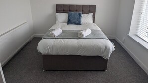 A neatly made bed with a grey headboard, white bedding, and a blue accent pillow. - Spacious 3BR Swansea House Near City Centre (Swansea)