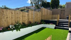 A well-maintained garden with a wooden fence, a white planter box with flowers, and a grassy area. - Spacious 3BR Swansea House Near City Centre (Swansea)