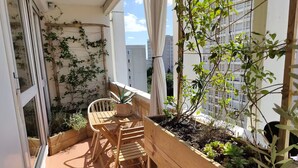 A small balcony with a wooden table and chairs, a potted plant, and a wooden planter box with succulents.