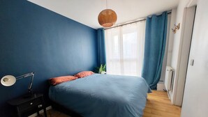 A bedroom with a bed, a nightstand, a lamp, and a window with curtains.